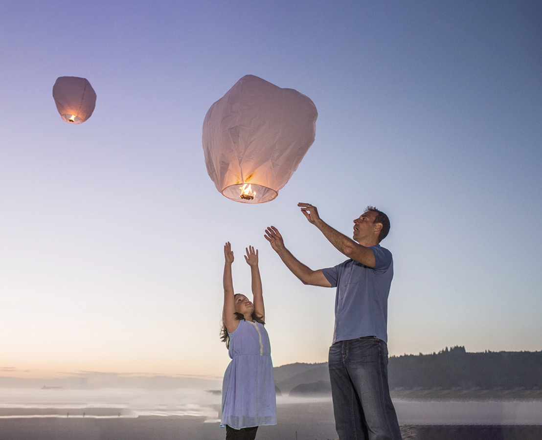 Otac i kći puštaju lampione na plaži pri zalasku sunca, simbolizirajući nadu, snove i nove početke