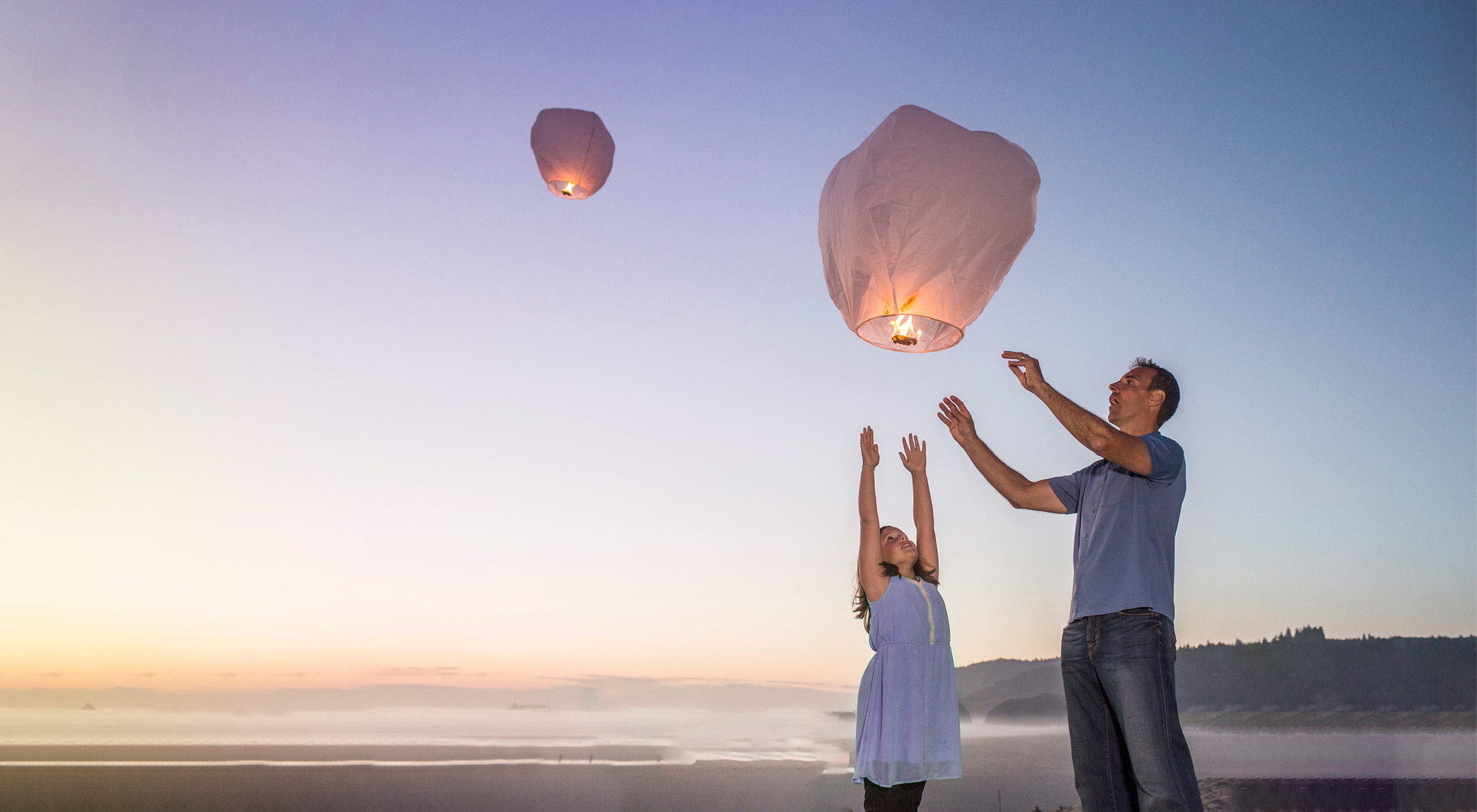 Otac i kćer puštaju leteće lampione u sumrak na plaži, simbolizirajući nadu i svjetliju budućnost